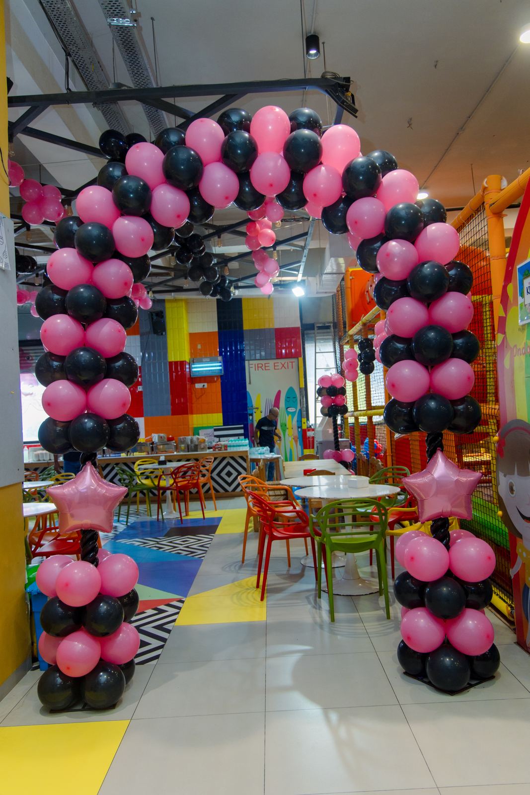 Pink and black balloon arch framing the café seating at Baccha Party Malad